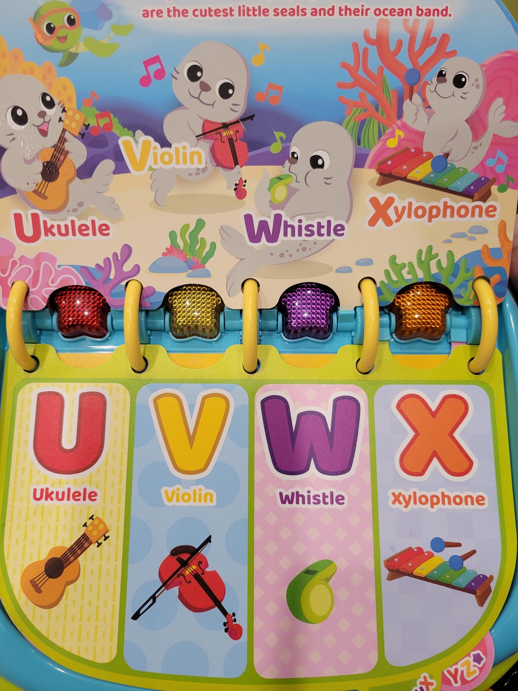 A picture of a children’s alphabet book with U for ukelele, V for violin, W for whistle, and X for xylophone and pictures of the respective objects.