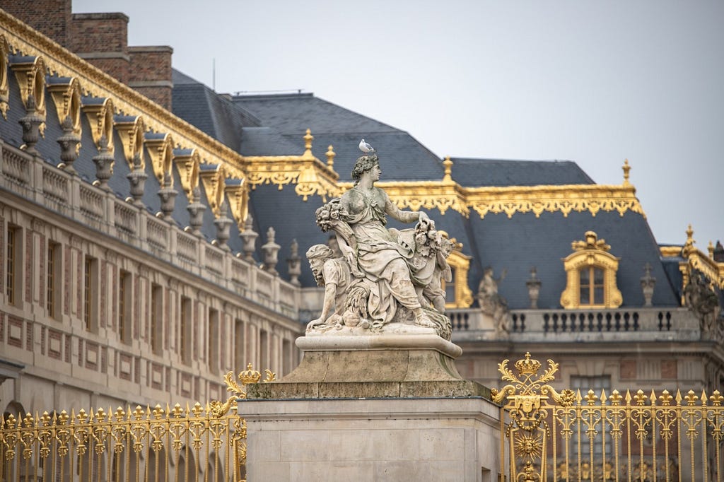 Gilded accents and a statue of a woman outside the Château de Versailles.