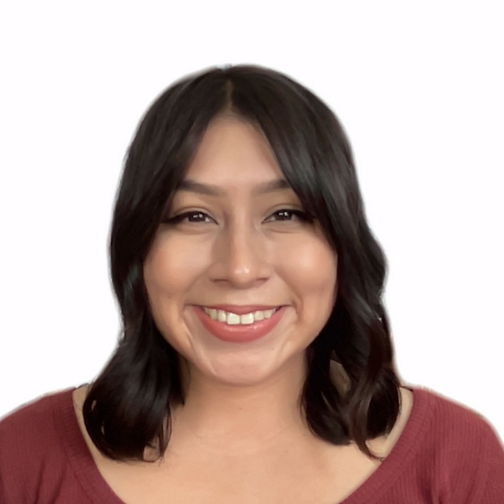 Photo of Yolis, a Hispanic woman, from the chest up. She is looking at the camera with an open-lipped smile. She is wearing a burgundy top. Her short brown curls are brushing both shoulders.