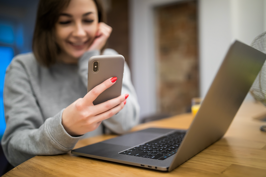 Mulher segura um celular enquanto esta em frente a um notebook