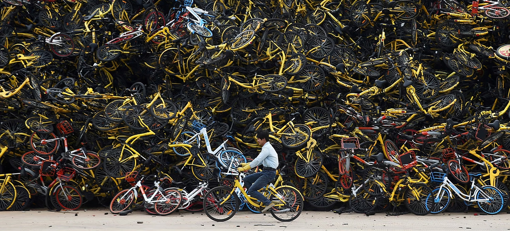 A worker rides a shared bicycle past a huge pile of unused shared bikes in a vacant lot in Xiamen, Fujian province, China, on December 13, 2017.