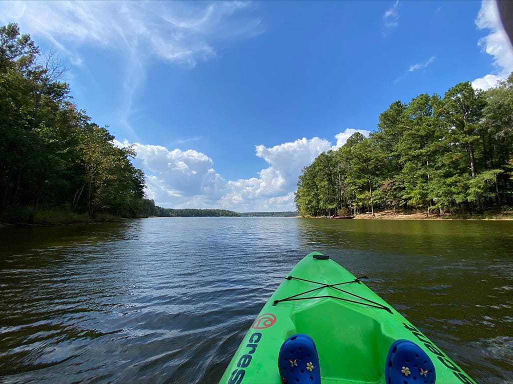 The front of the kayak, with two water shoes peeking out from the bottom and vast openness of the lake in front.
