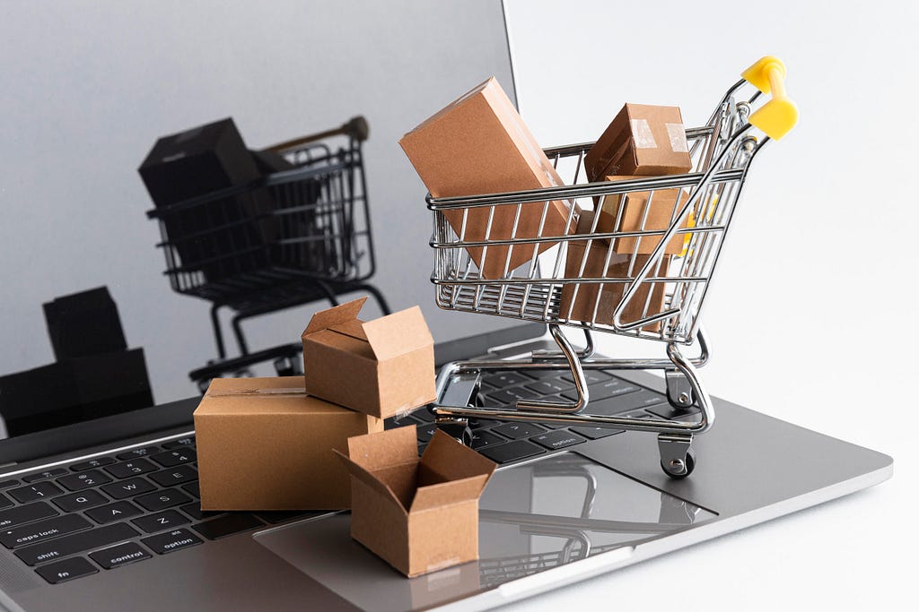 An open notebook in a white background, with a shopping cart full of cardboard boxes standing for the increasing of sales in ecommerce.