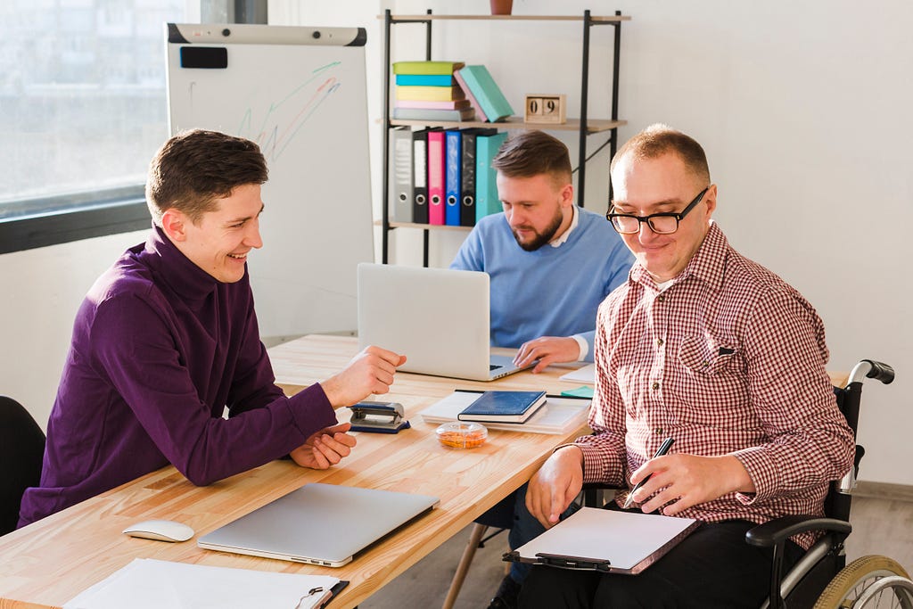 Three men working in an office. One of them is in a wheelchair.