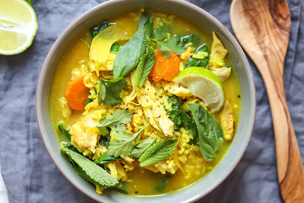 Bright bowl of ginger and turmeric chicken soup with rice and leafy vegetables.