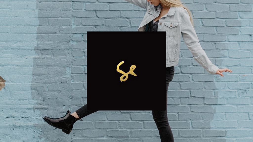 blonde woman walking making big steps ahead of a light blue brick wall, in the foreground is the album cover of Sylvan Esso, by duo Sylvan Esso