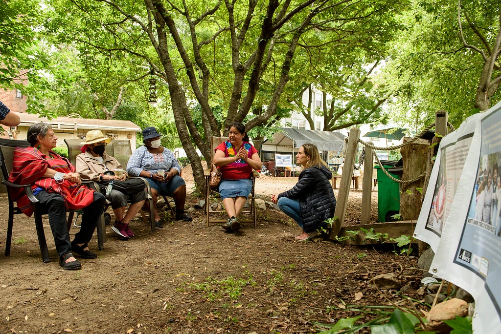 A group seated in the park, in conversation next to project banners