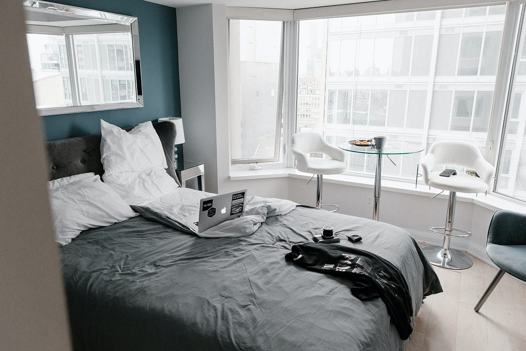 Hotel room with laptop in unmade bed and breakfast on table