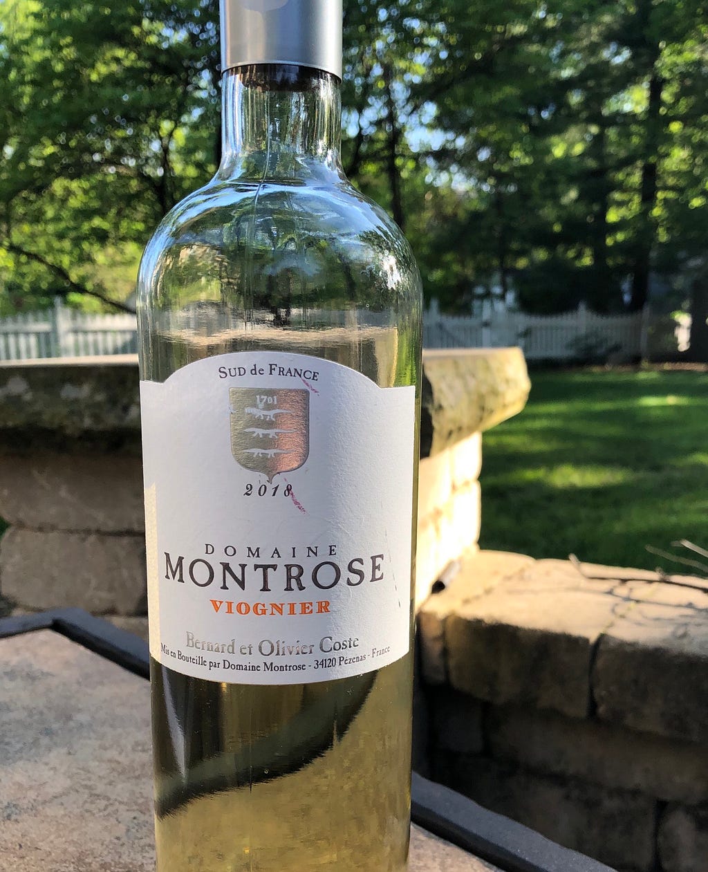 A bottle of white wine — Domain Montrose Viognier — in a backyard in the afternoon sun.