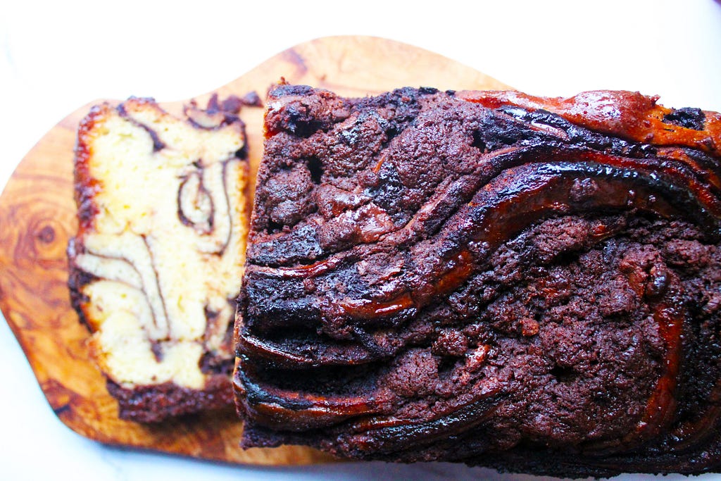 Chocolate babka loaf viewed from above on a wooden chopping board. A slice shows the inside chocolate swirls of the cake.