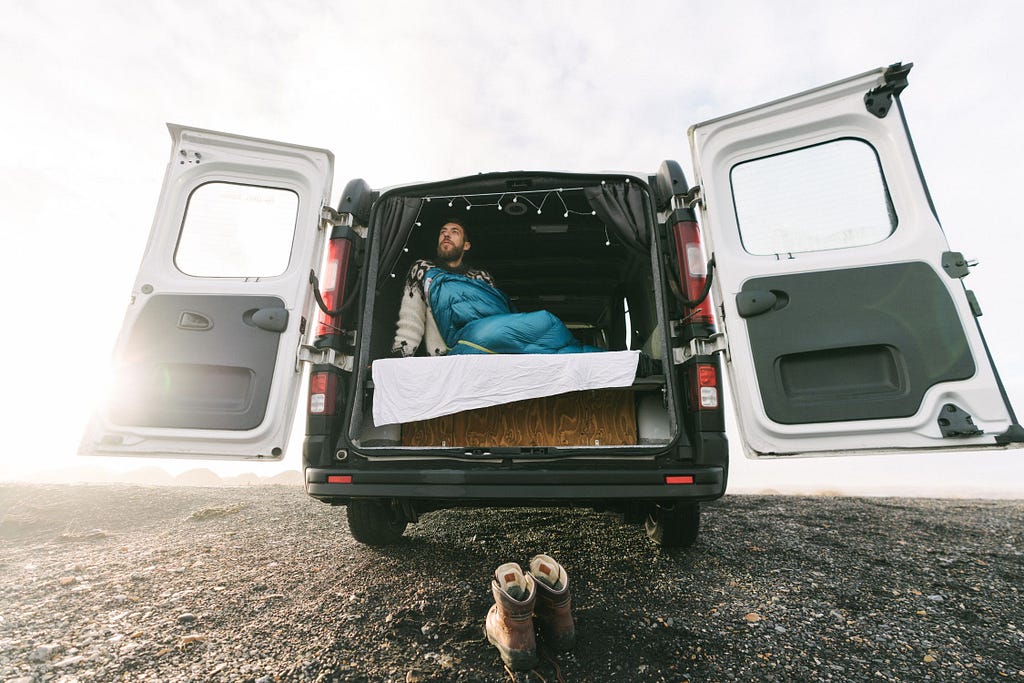 Man in sleeping bag in the back of a microcamper with doors open