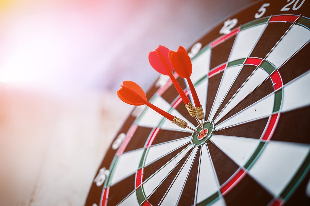 Three darts that have all hit the bulls-eye center target of a dart board.