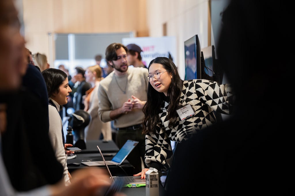 A woman standing behind a table talks to a group of people.