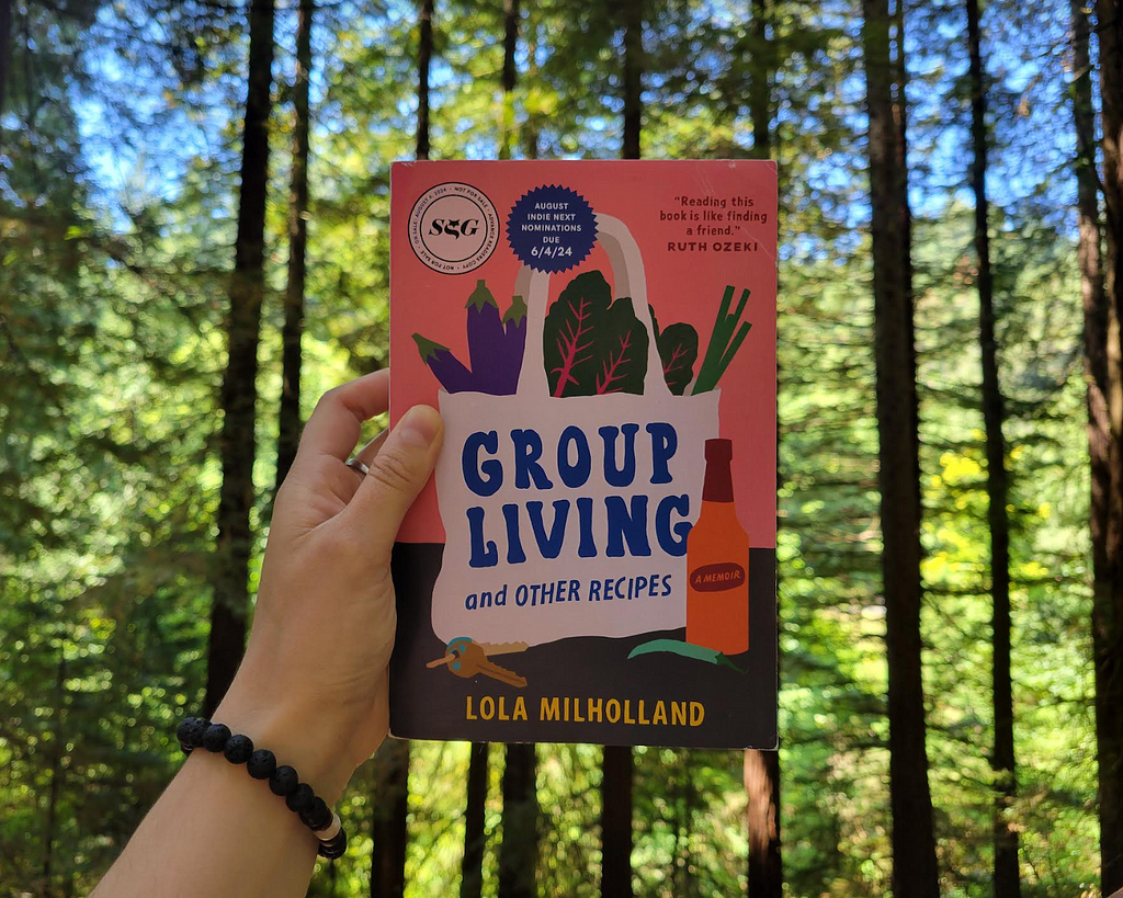 Milholland’s book is held in center frame against a backdrop of redwood trees. Its title is displayed on the image of a produce-filled shopping bag