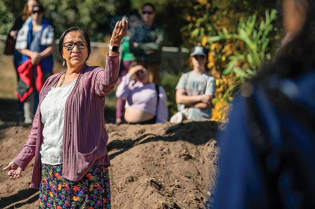 Nidawin Preston holds aloft burning herbs as participants look on in the Regis garden during Climate Action Day