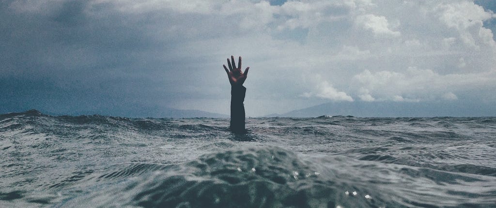 A hand reaching up out of the water, seemly alone in the middle of a large body of water on a turbulent day.