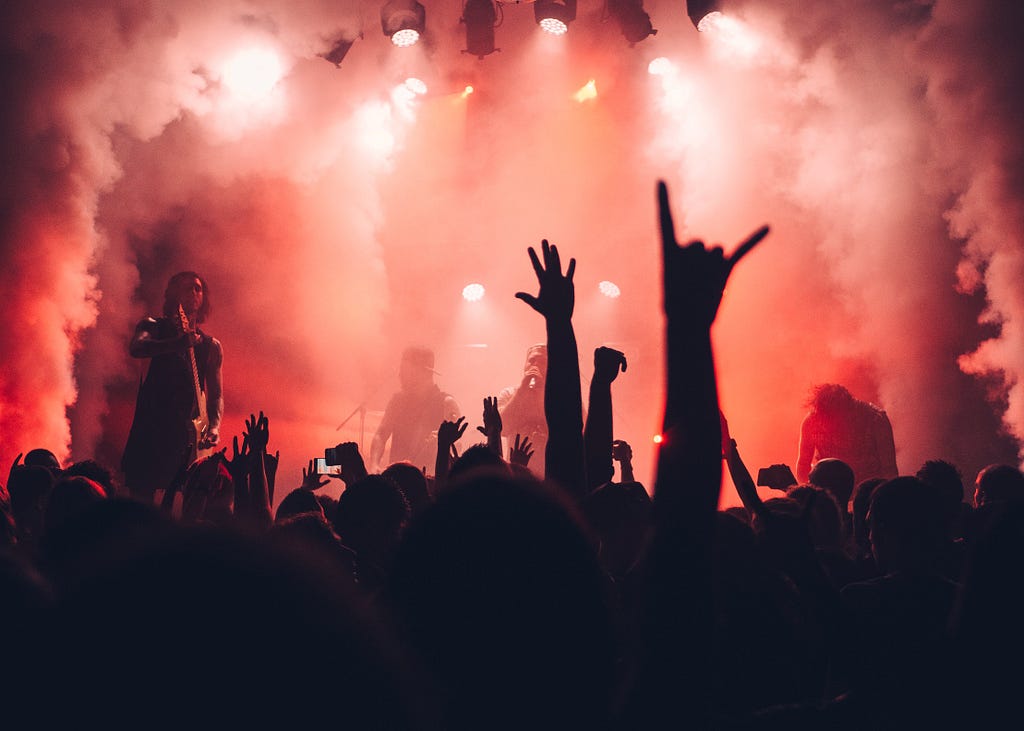 A Band on stage and a crowd with hands in the air