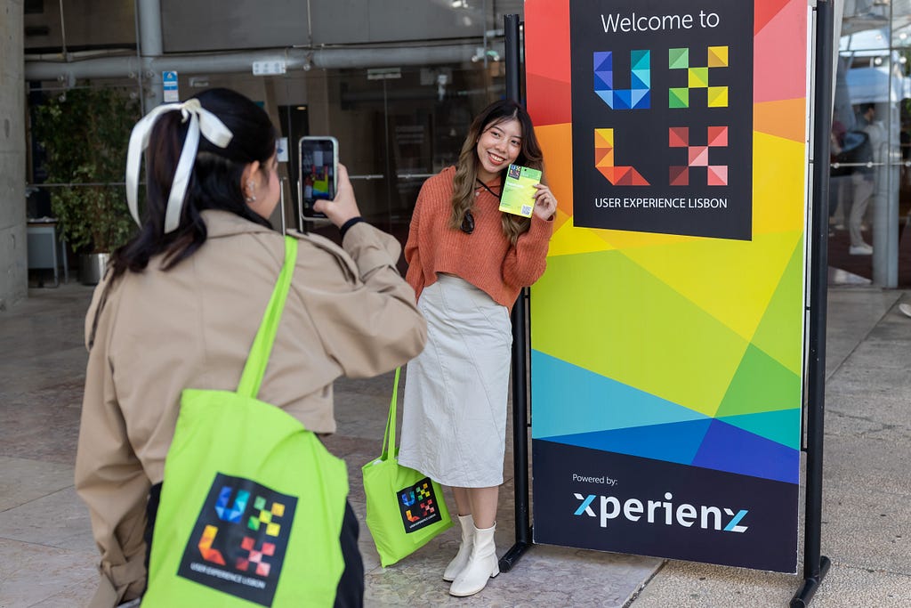 Two attendees taking photos by the “Welcome to UXLx” sign at the venue entrance.