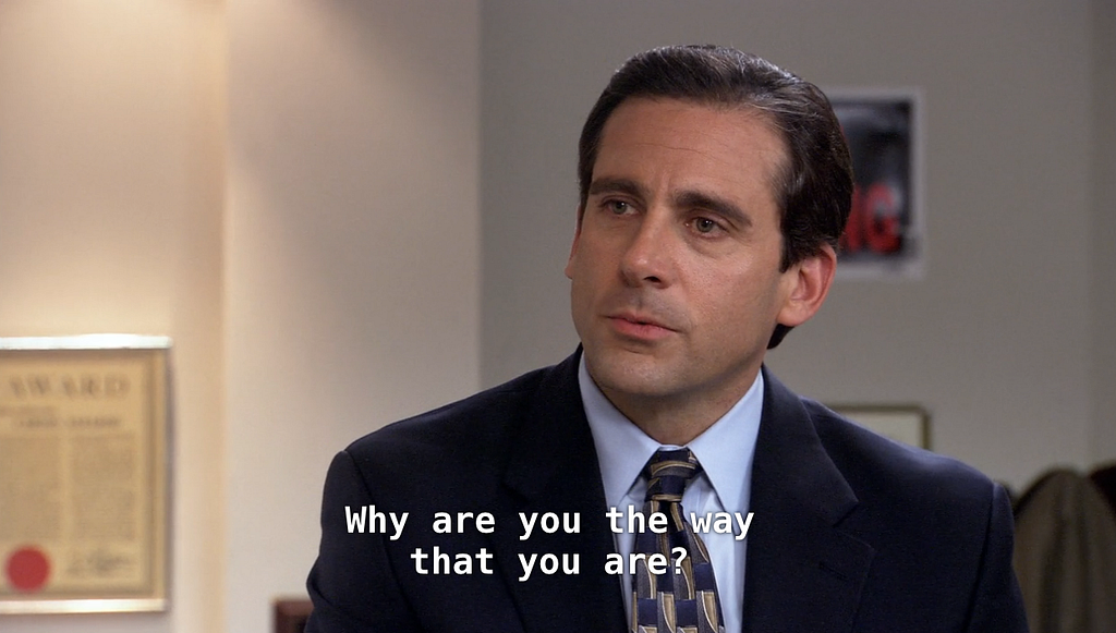 Michael Scott, personagem de The Office, vestindo um terno, camisa e gravata perguntando: “Why are you the way that you are?”