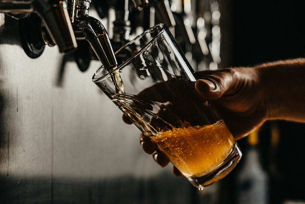 Torneira de bar servindo cerveja puro malte em um copo de vidro segurado por uma mão.