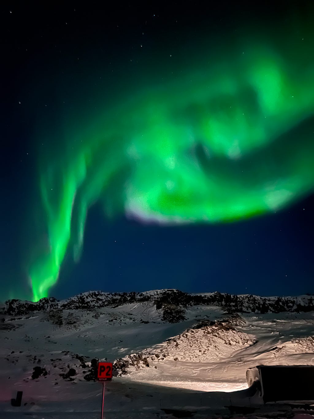 A mountain of snow with green Northern lights in the background.