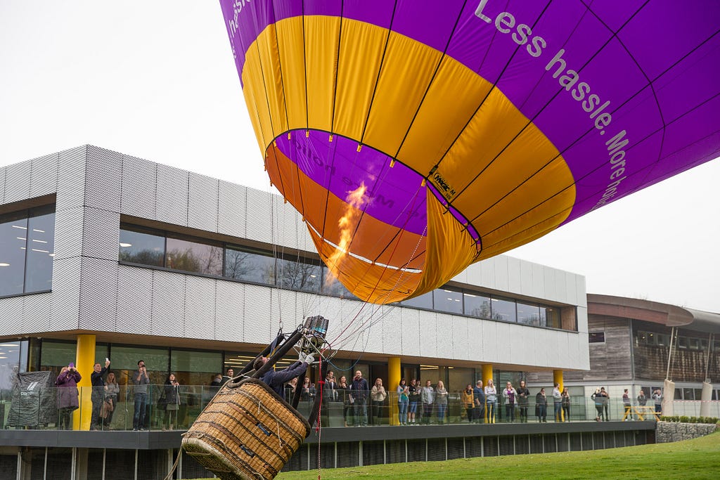 A purple Holiday Extras hot air balloon takes off from in front of ther Holiday Extras offices