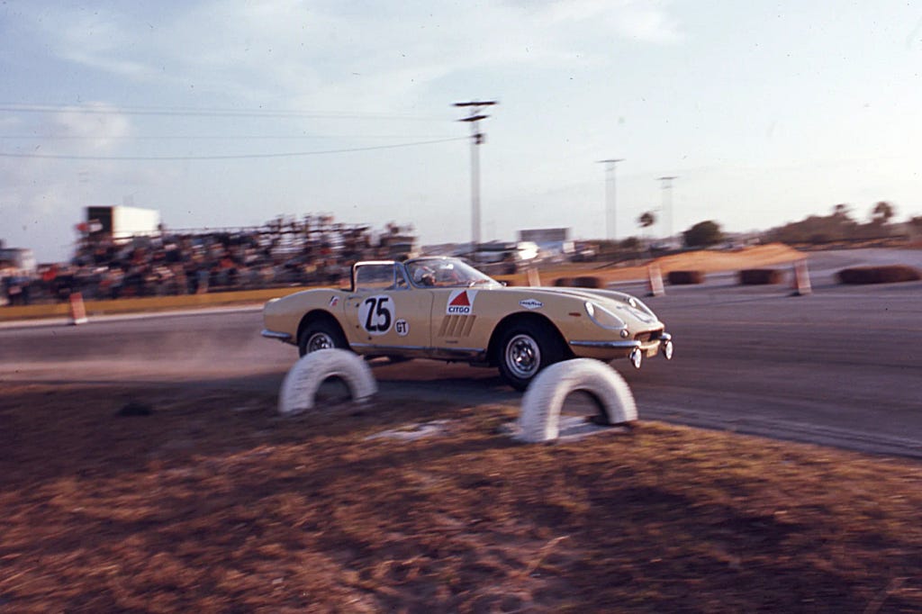 An antique yellow racecar with the number 25 on its side speeds down a racetrack. Everything but the car is slightly blurry in the photo.