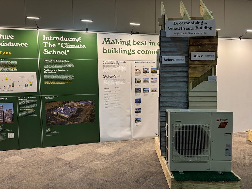 photo showing the back wall of educational panels; in the foreground is a section of a mock house wall and a Mitsubishi heat pump.