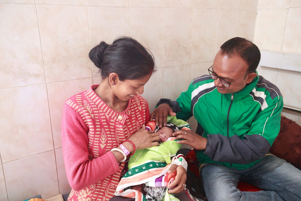 A new mother and father admire and stroke their newborn as the mother cradles their baby in her arms.