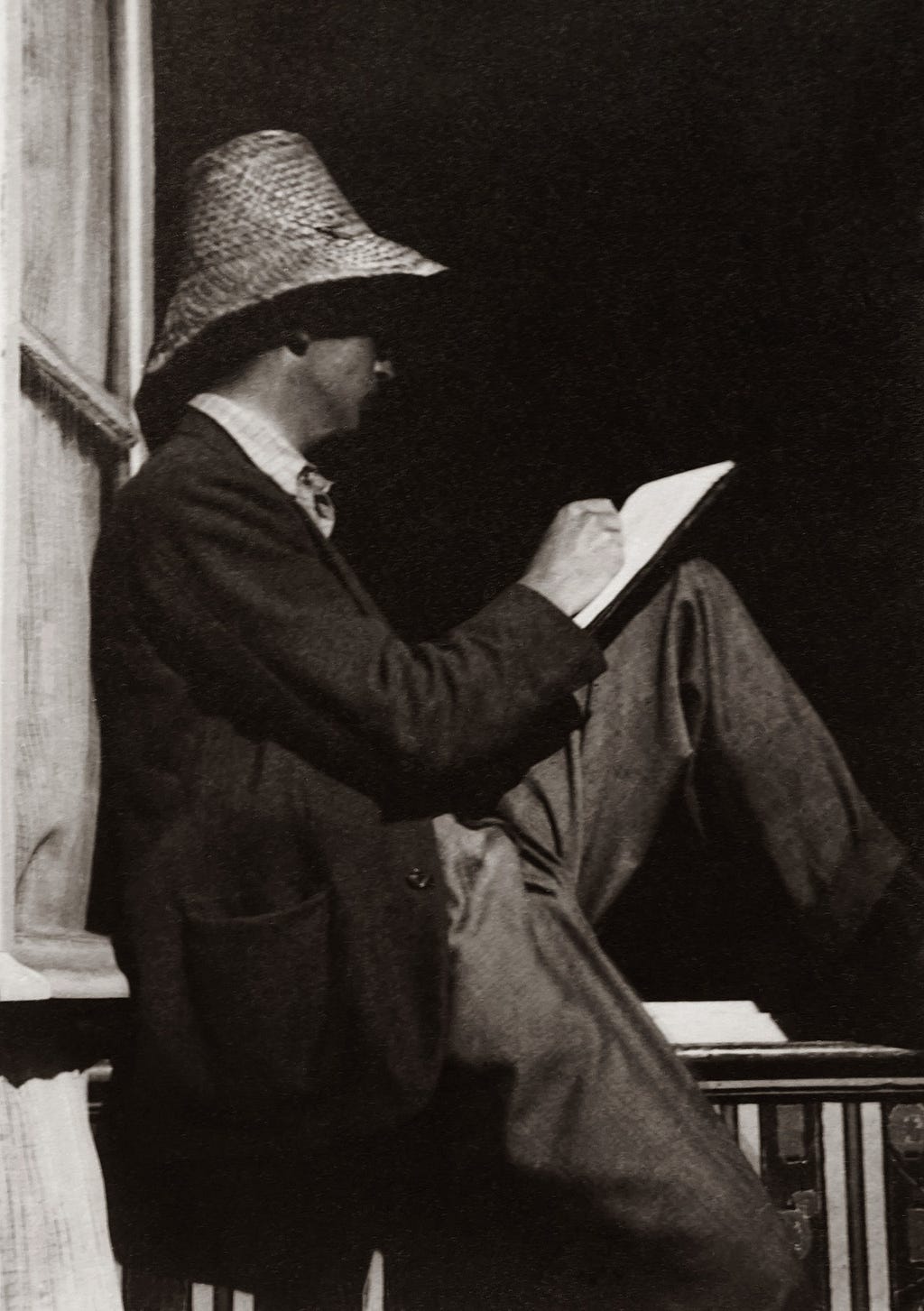 A man sitting on headrails, wearing a hat, and writing on a notebook
