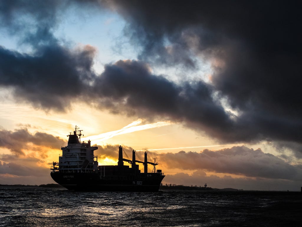 An ocean tanker under dark clouds and sunlit vapour trails