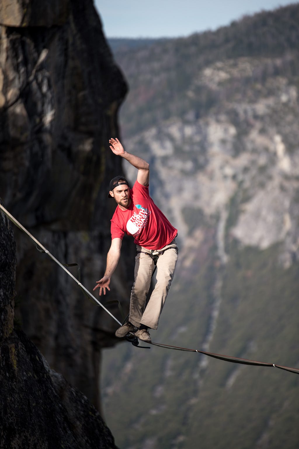 Man effortfully keeping balance on a tight rope between cliff faces with a very steep drop