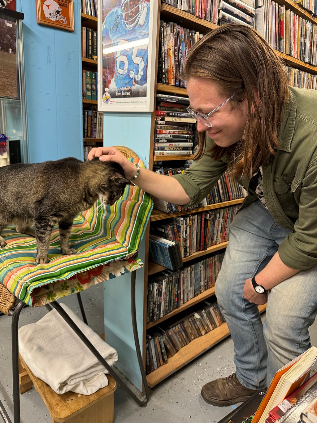 A person pets a cat’s head in front of a bookshelf at The Book Cellar in Temple, Texas.
