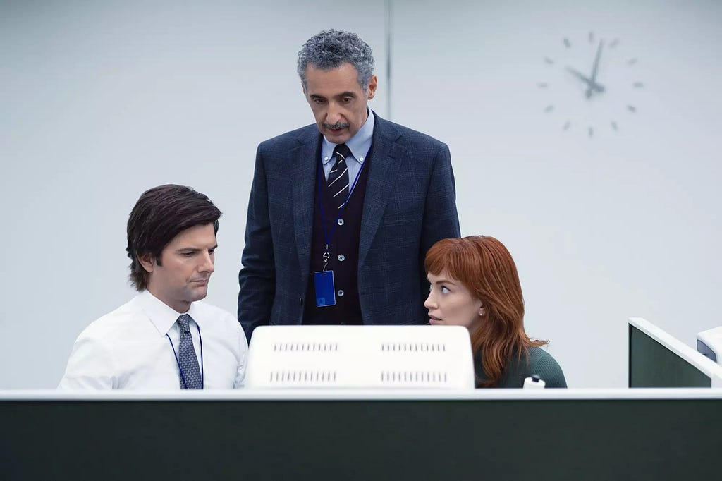 A middle aged man, an older man, and a young woman look at a CRT monitor with concern in a minimal white office