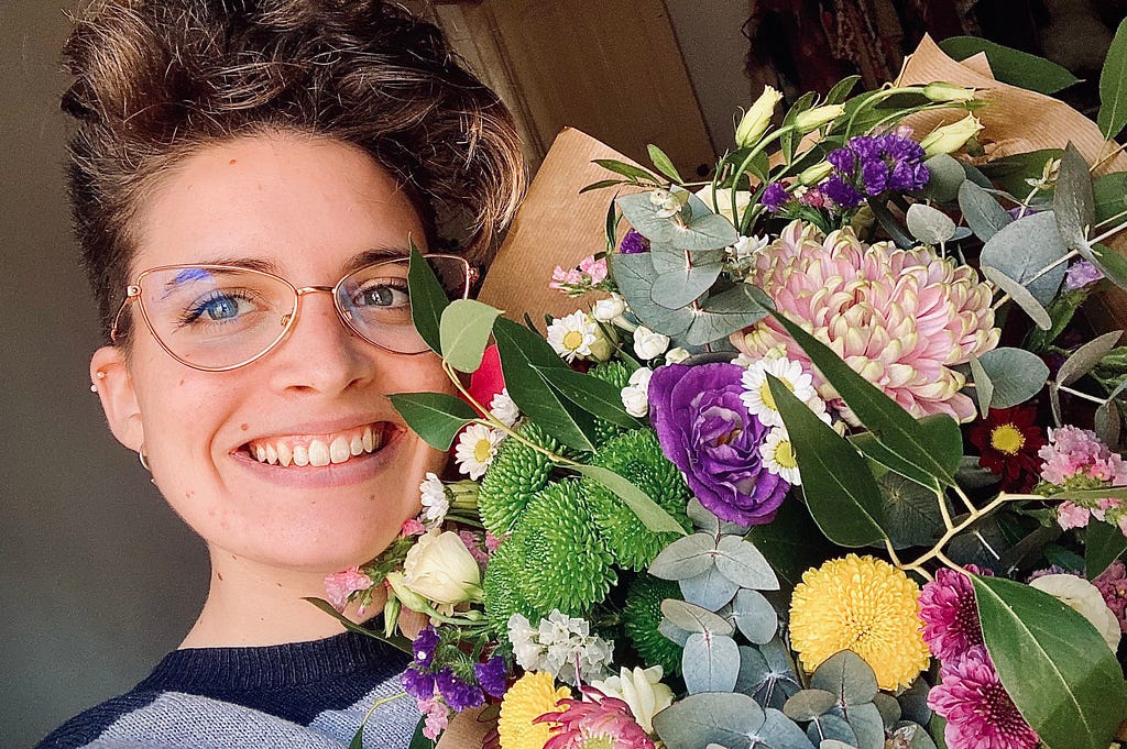 Woman wearing glasses and smiling holding a large bouquet of colorful flowers.