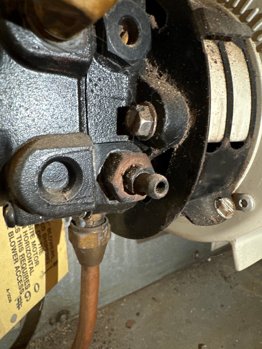 Detailed view of a Beckett oil burner’s pump and coupling assembly, highlighting the copper supply line and adjustment screws. The components show signs of wear and oil residue, indicating frequent use and the need for maintenance.