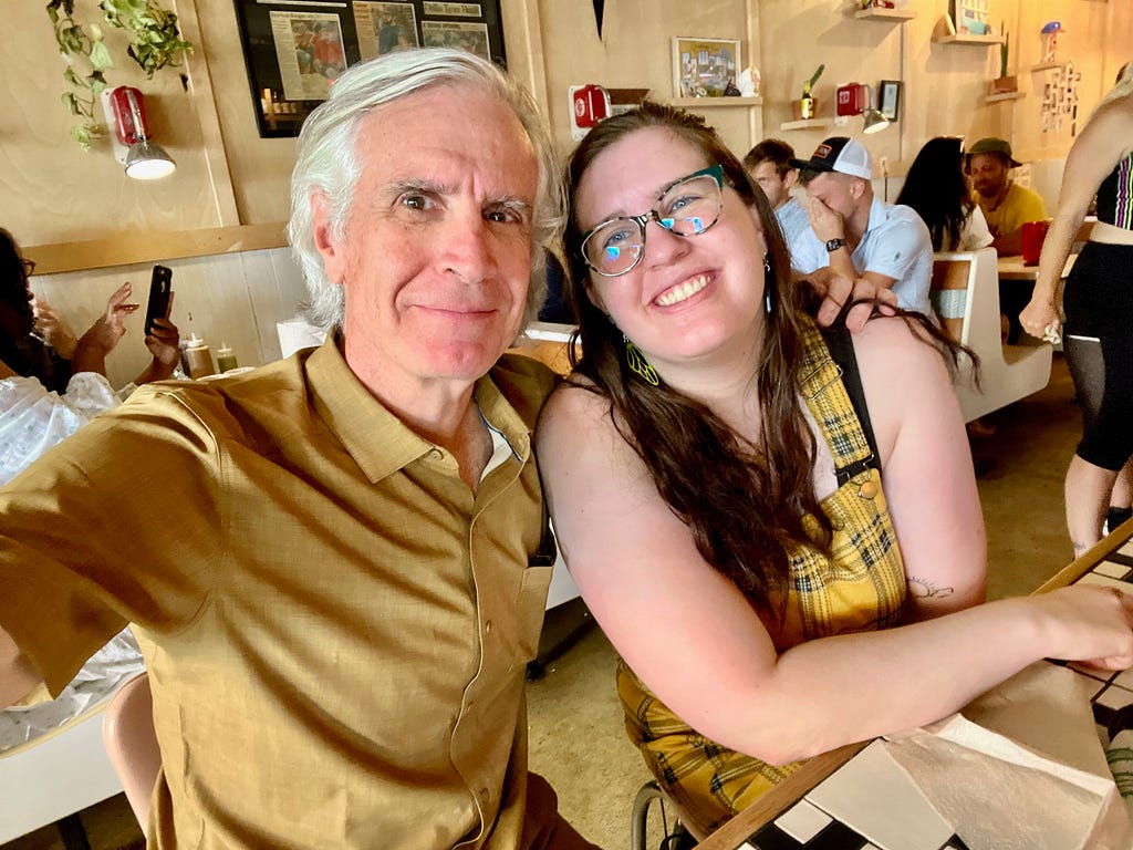 And older man and his 20-something daughter dressed in yellow sit in a cafe