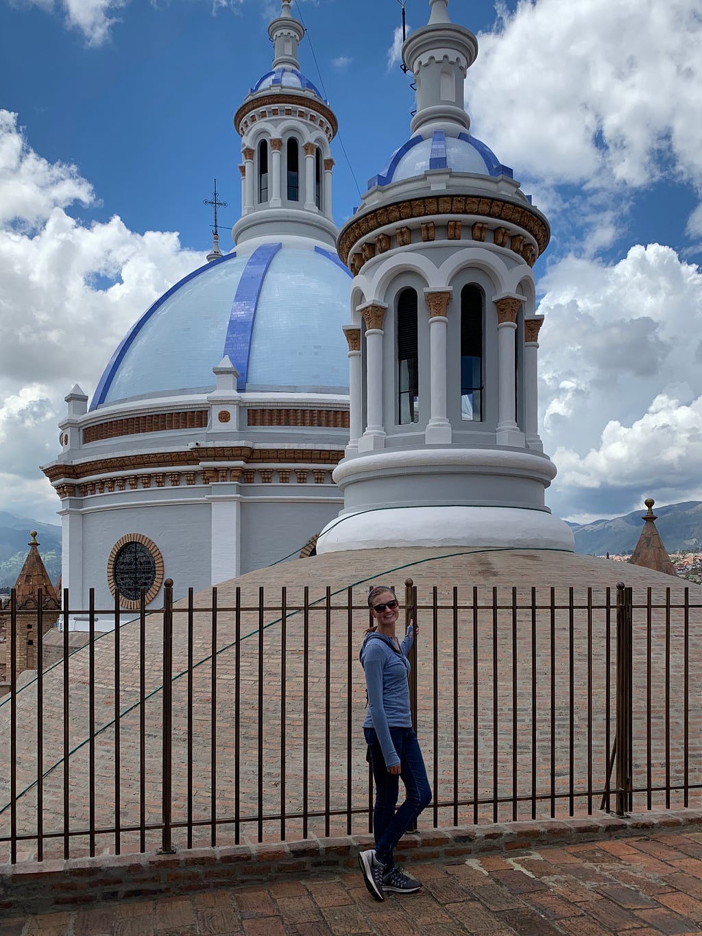 Woman standing in front of Cuenca’s Cathedral sky blue domes set against a blue sky with fluffy white clouds.