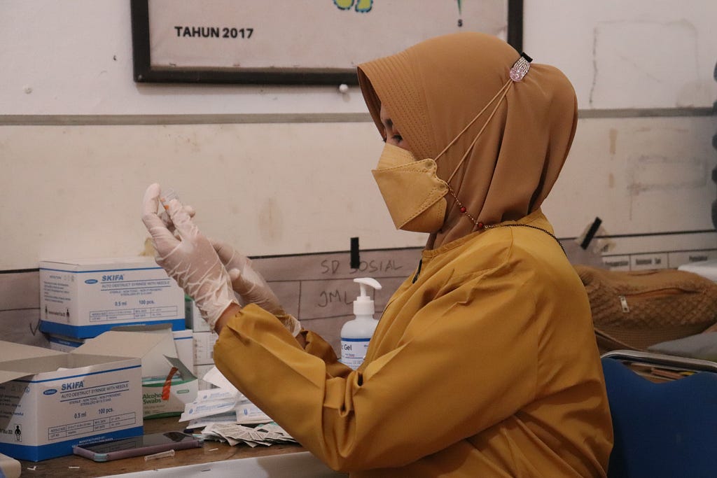Woman wearing PPE handling vaccine.