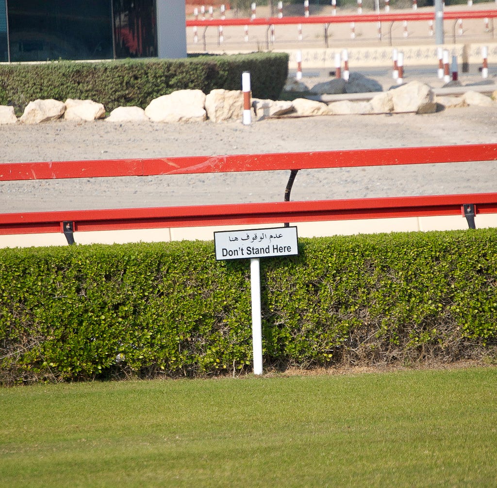 Sign post on the edge of a camel race track outside of Dubai, UAE, that reads “Don’t Stand Here.”