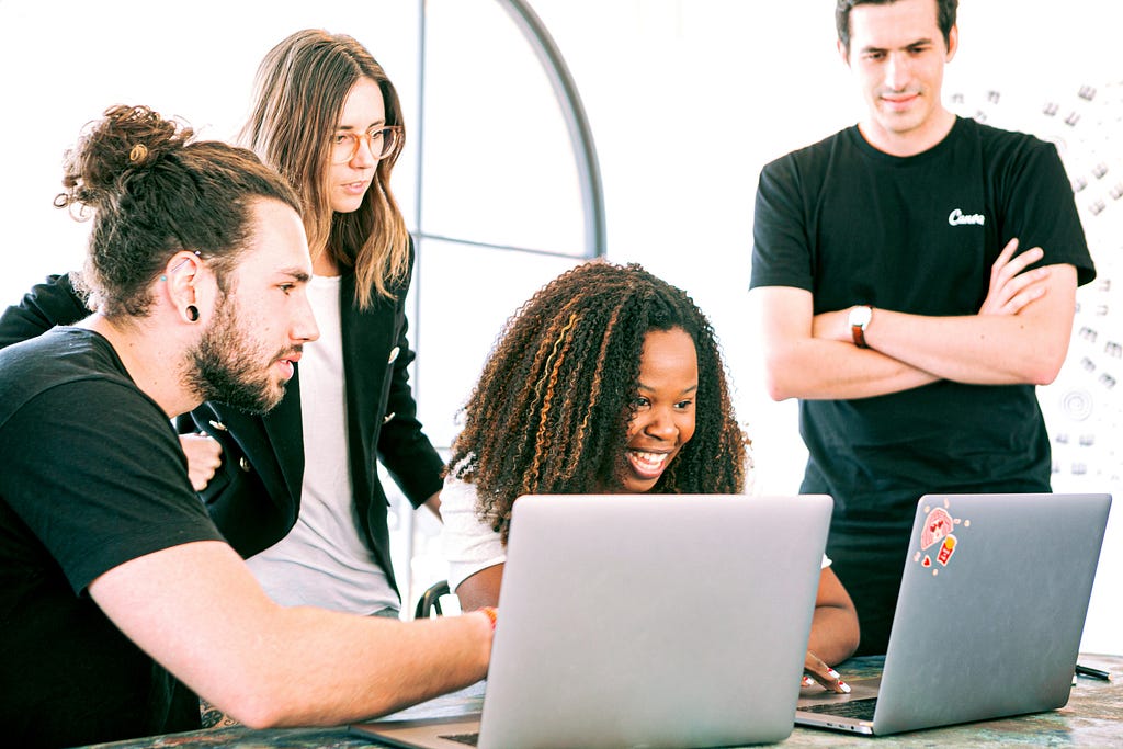 Five people behind two laptops in a brightly lit office, all clothed black and white.