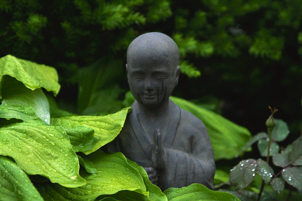 There is a statue of a mediating monk carved in stone in between leaves.