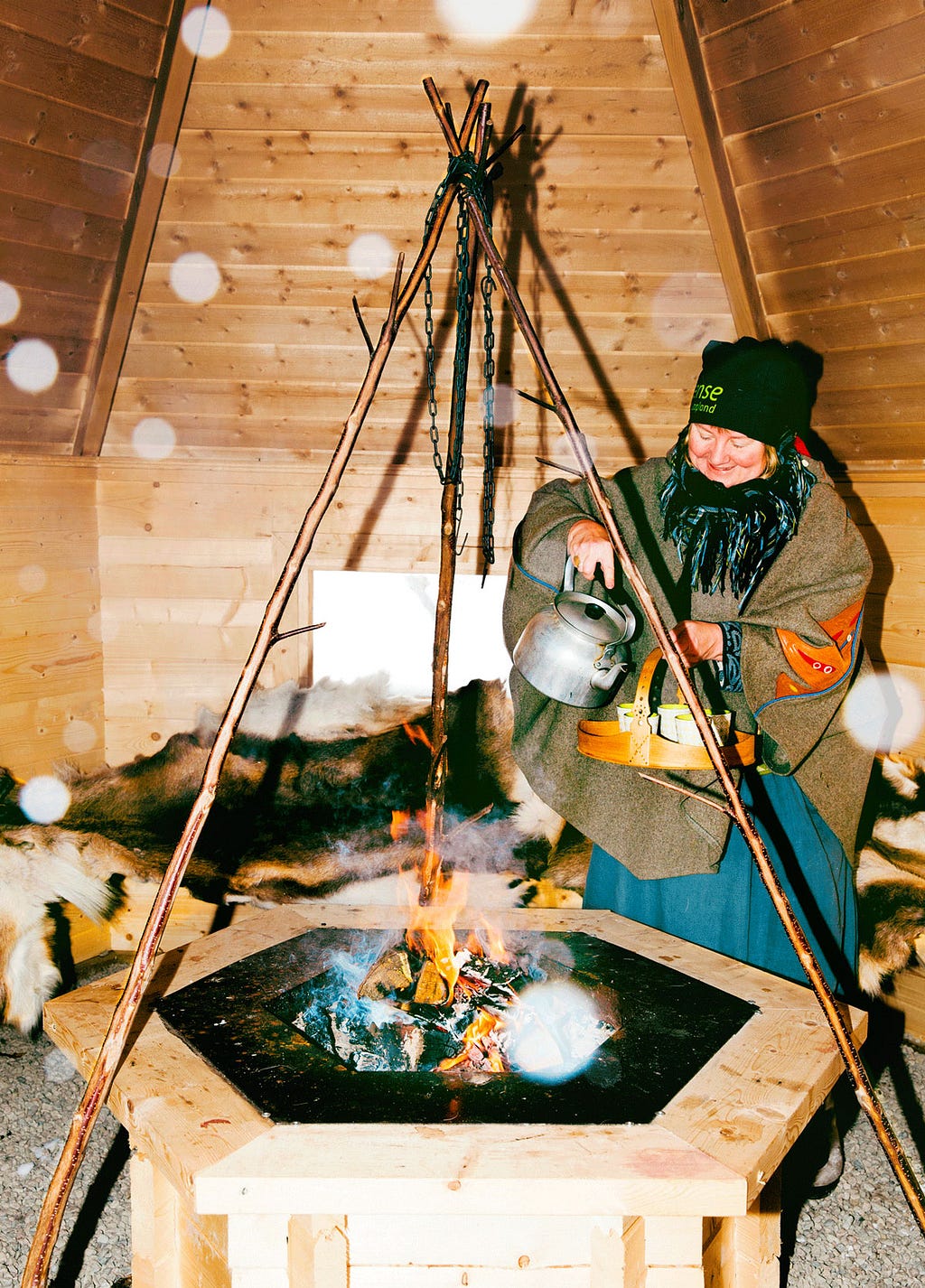 A woman prepares hot tea inside a Sámi kåta.