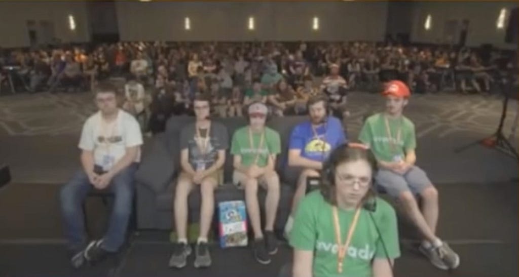 A picture from a GDQ live stream. The speedrunner is sat closest to the camera, followed by the couch, then the audience.