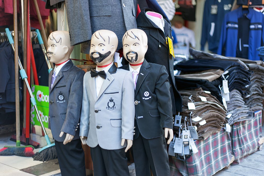 three child size mannequins with facial hair drawn on by sharpie in a market setting