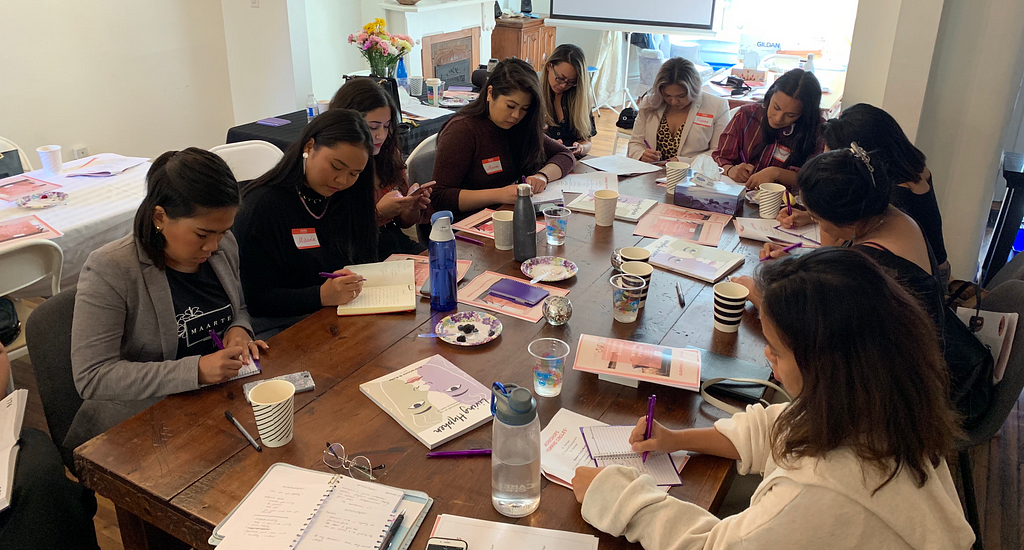 Group of women sitting around a table writing.