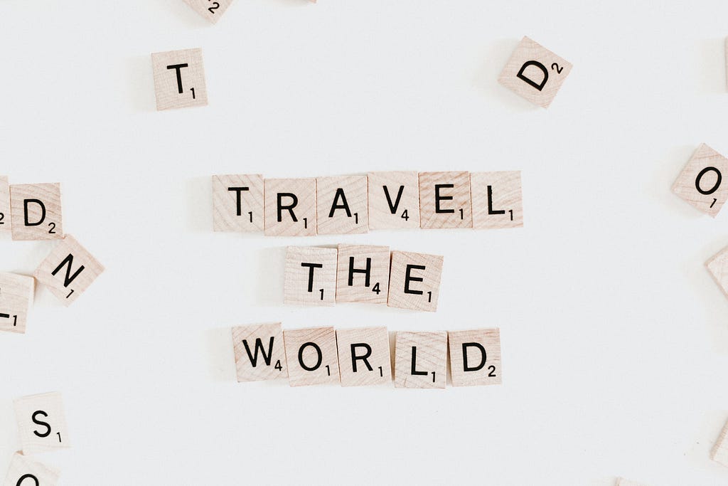 Wooden tiles spelling put “Travel the world” on a white backdrop.
