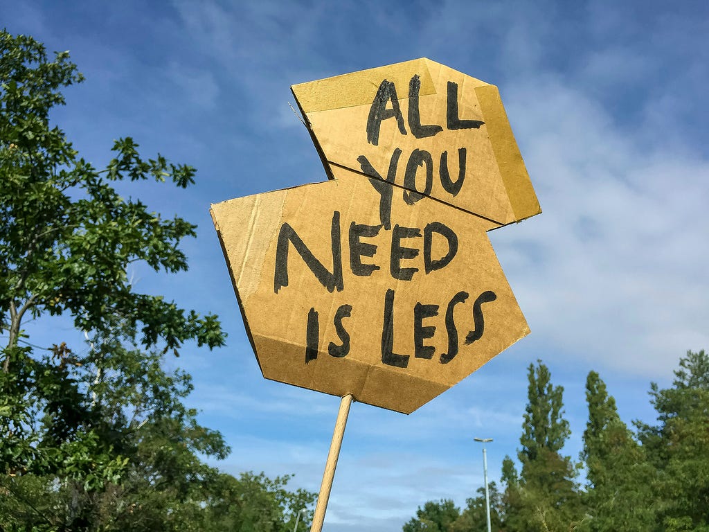 A carboard sign that says “All you need is less”