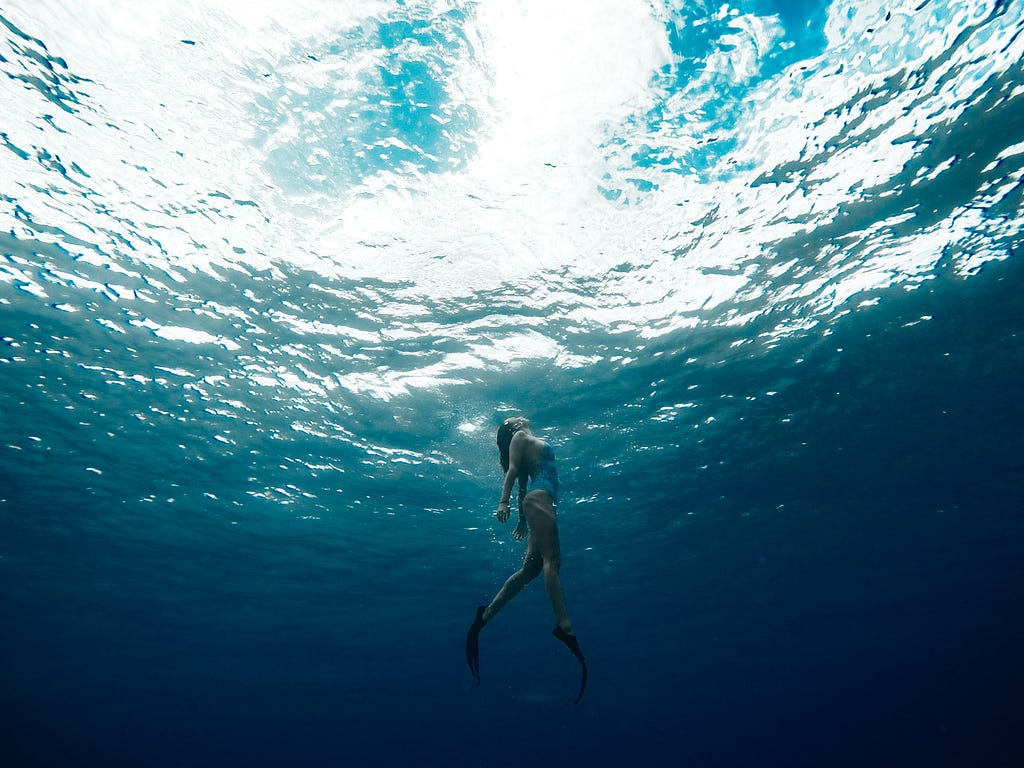 Woman under the sea swimming towards the light above the surface.