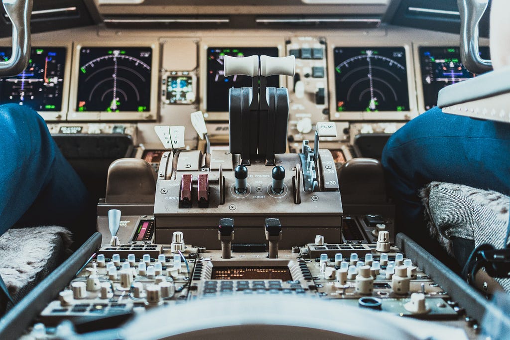 A plane dashboard with lots of buttons and levers, and a pilot and copilot